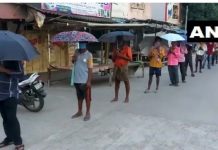 शराब लेने के लिए छतरियों के साथ खड़े हुए लोग