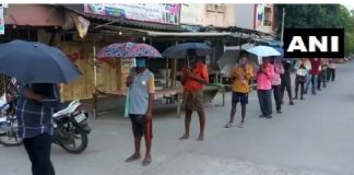 शराब लेने के लिए छतरियों के साथ खड़े हुए लोग
